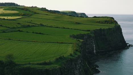 Toma-Aérea-En-Ascenso-De-Escarpados-Acantilados-De-Irlanda-Del-Norte-Con-Campos-Verdes