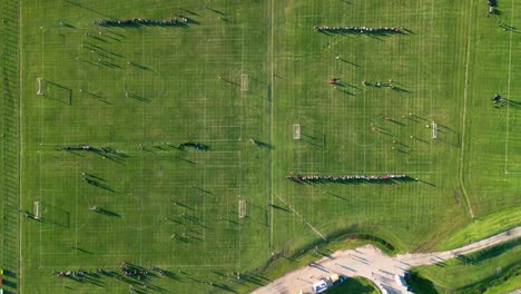 Vista-Aérea-De-Arriba-Hacia-Abajo-En-Movimiento-Lento-De-Personas-Jugando-En-Tres-Campos-De-Fútbol-En-Un-Día-De-Verano-Al-Atardecer