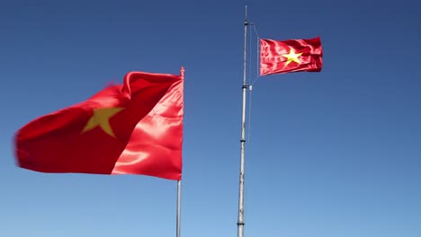 Two-vietnamese-flags-flapping-in-the-wind-on-top-of-Fansipan,-the-highest-mountain-in-Indochina-located-in-Sapa,-Vietnam