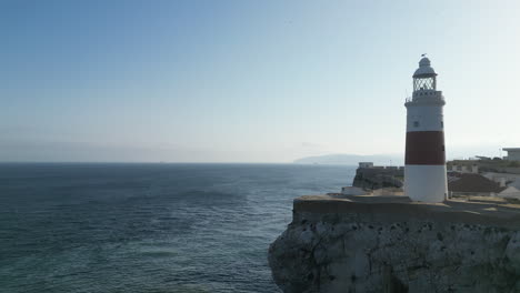 4K-Drohnenaufnahme,-Die-über-Dem-Ozean-Aufsteigt-Und-Nach-Rechts-Schwenkt,-Um-Den-Felsen-Von-Gibraltar-Und-Seinen-Leuchtturm-Bei-Sonnenuntergang-Zu-Zeigen