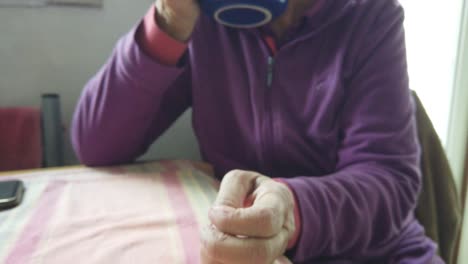 Senior-lady-drinks-hot-tea-smoking-pot-warming-her-hands-in-vintage-living-room