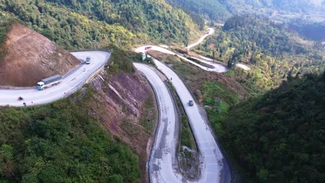 This-drone-footage-captures-the-winding-mountain-roads-of-Ha-Giang-in-North-Vietnam,-featuring-vehicles-navigating-the-sharp-curves-and-dramatic-elevation-changes