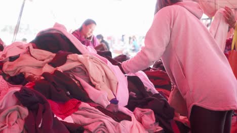 Person-looks-for-a-sweater-among-a-large-pile-of-used-clothes-in-a-crowded-flea-market