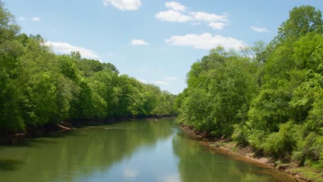 Slow-flowing-river-lined-with-lush-dense-forest-trees-and-thicket