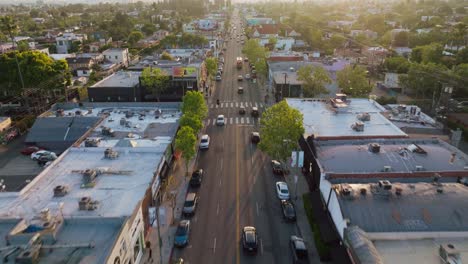 Drone-Flying-Above-Cars-on-Busy-Melrose-Avenue,-Afternoon-Sunlight-Ahead-with-City-Skyline-on-Hazy-Horizon