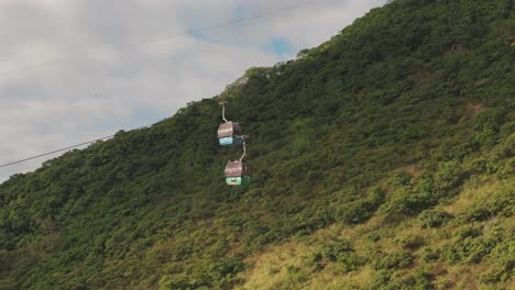 Drone-view-with-a-telephoto-lens-of-two-Cable-Cars-or-Gondolas-traveling-through-a-green-mountain-in-the-city-of-Salta,-Argentina