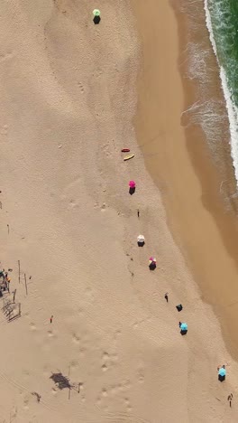 Aerial-view-of-ocean-waves,-golden-sand,-and-umbrellas-on-the-beach