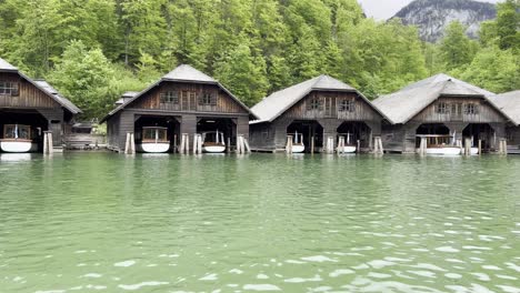 Boat-ride-passing-by-the-wooden-boat-sheds-at-picturesque-Lake-Königssee-near-Berchtesgaden-in-the-Bavarian-Alps-in-Germany