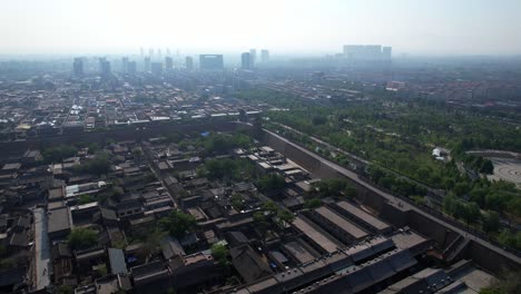 Aerial-view-of-Pingyao,-historic-walled-old-town-with-modern-tall-buildings-in-the-hazy-background