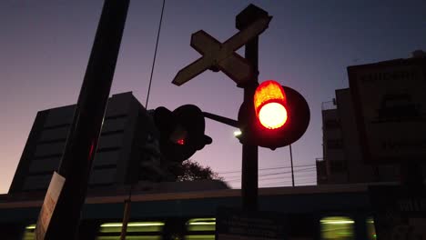 Red-lights-blinking,-sunset-night-train-passing-by-background-skyline-downtown