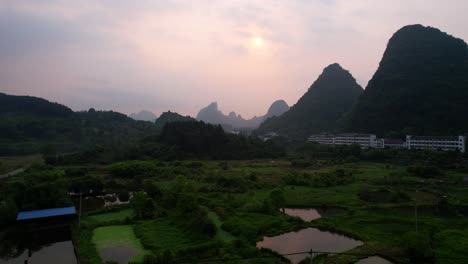 Die-Sonne-Spiegelt-Sich-Im-Wasser,-Während-Eine-Drohne-Bei-Sonnenaufgang-In-Yangshuo,-China,-Auf-Die-Berge-Von-Guilin-Zufliegt