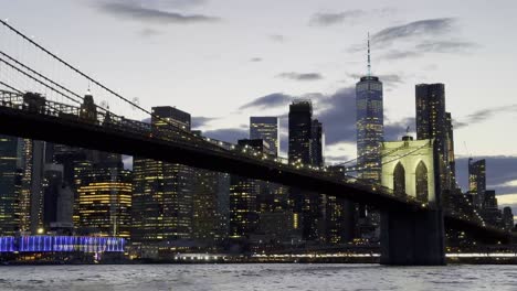 Una-Impresionante-Vista-Del-Puente-De-Brooklyn-Iluminado-Por-La-Noche,-Con-Las-Vibrantes-Luces-Del-Horizonte-De-Manhattan-Creando-Un-Deslumbrante-Telón-De-Fondo-Sobre-El-East-River