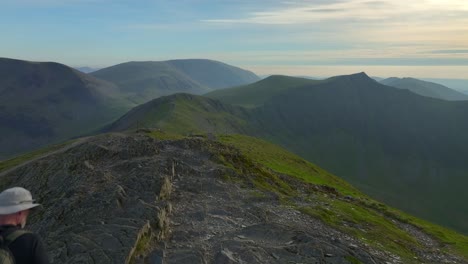 Mountain-walker-arriving-on-summit-with-view-to-rugged-silhouetted-peaks-and-ridges