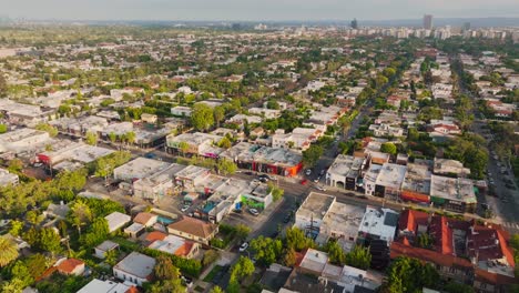 Aerial-Shot-of-West-Hollywood-on-Sunny-Day,-Cars-Driving-Through-Tree-Lined-Streets-and-Buildings-on-Horizon