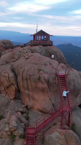 Vertical-Aerial-View-of-Woman-Walking-on-Stairways-on-Top-of-Mountain-Peak-to-Hilltop-Cottage,-Devil's-Head,-Colorado-USA