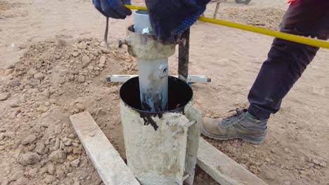 African-construction-worker-installs-and-measures-concrete-pile-frame-mould-and-support-for-solar-PV-concrete-pile,-Gambia---close-up