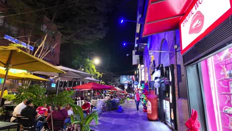 Bustling-nightlife-scene-in-El-Poblado,-Medellin-with-vibrant-signs-and-outdoor-seating-at-night