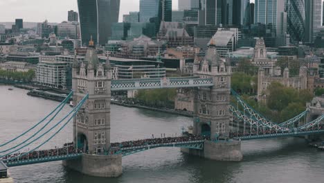 Toma-En-ángulo-Lento-Y-Circular-De-Corredores-De-Maratón-En-El-Tower-Bridge-Con-Edificios-Emblemáticos