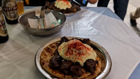 Grilled-Meat-with-Cream-on-Flatbread-and-Beer-Bottles-at-Restaurant-Table