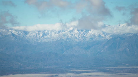 Majestätischer-Blick-Auf-Schneebedeckte-Berge,-Die-Teilweise-Von-Wolken-Bedeckt-Sind,-Im-Joshua-Tree-Nationalpark,-Mit-Einem-Riesigen-Tal-Im-Vordergrund