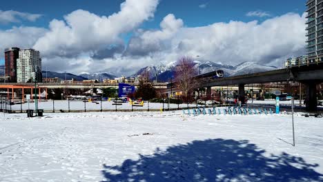 The-Skytrain-in-Snowy-Vancouver-Park-passes-on-Elevated-Rail-Tracks---Sunny-Winter-Daytime-View-of-Public-Transit-and-Mountains