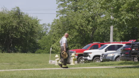 Firefighter-walking-on-grass-near-fire-hydrant-and-emergency-vehicles-on-a-sunny-day