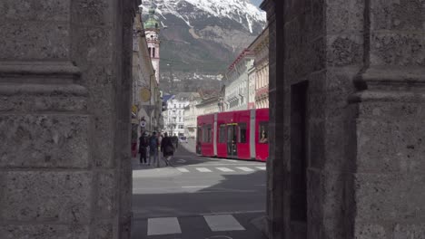 A-tram-driving-down-Maria-Theresien-Street,-viewed-through-one-of-the-arches-of-the-Triumphal-Arch,-Innsbruck,-Tirol,-Austria