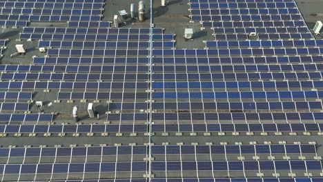 Toma-Aérea-De-Los-Paneles-Solares-En-El-Techo-De-Un-Edificio-De-Producción-En-Un-Día-Soleado