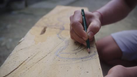 A-close-up-shot-of-a-Balinese-maskmaker's-hands-sketching-the-pattern-for-a-traditional-Balinese-mask,-known-as-Barang-Bangkung,-onto-the-sacred-wood