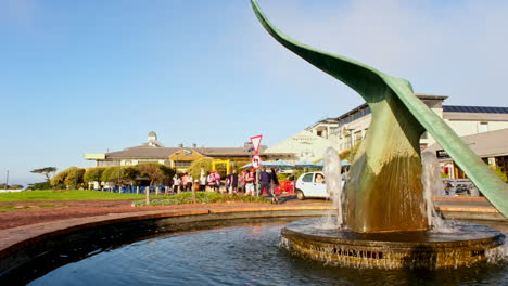 La-Gente-Pasa-Junto-A-La-Icónica-Fuente-De-Cola-De-Ballena-En-Hermanus-Cbd,-Cerca-De-Restaurantes