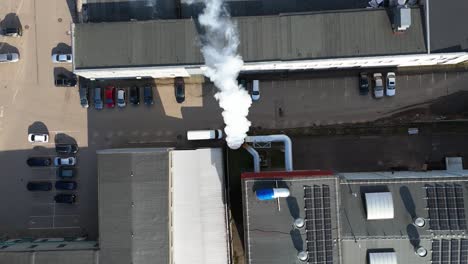 Drone-shot-of-the-white-smoke-rising-from-a-factory-chimney-on-a-sunny-day,-top-down-shot