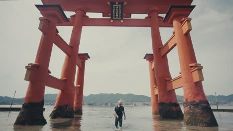 Man-Walking-Through-Floating-Torii-Of-Itsukushima-Shrine-On-Miyajima-Island-In-Japan