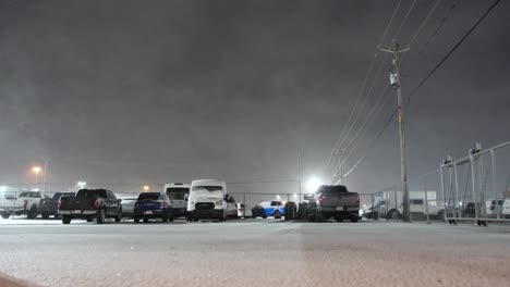 Snowfall-drifts-across-the-night-sky-above-parking-lot