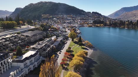 Colourful-Fall-season-in-Queenstown,-Aerial-view-of-lakeshore-with-hotels,-sunny-day-in-New-Zealand