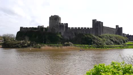 Couple-rowing-a-boat-in-a-lake-in-front-of-Pembroke-Castle-facade,-Wales