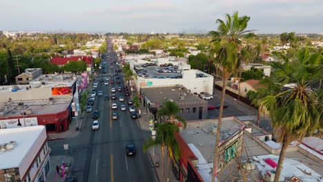 Toma-Aérea-De-West-Hollywood-Durante-El-Día,-Autos-En-La-Avenida-Melrose-Bordeada-De-Palmeras,-Visto-Desde-Arriba