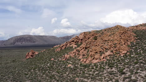 Aerial-view-of-Crater-Mountain-and-Aeolian-Buttes-along-Highway-395-in-California,-showcasing-rugged-red-rock-formations-against-a-backdrop-of-expansive-desert-and-mountainous-terrain