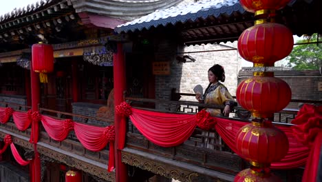 Pretty-Qing-girl-fanning-herself-and-smiling-on-balcony-with-decorations-in-Pingyao,-China