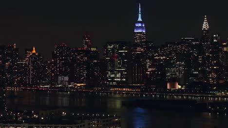 An-aerial-view-at-night-over-Long-Island-City,-Queens-with-the-Eastside-of-New-York-City-in-the-background