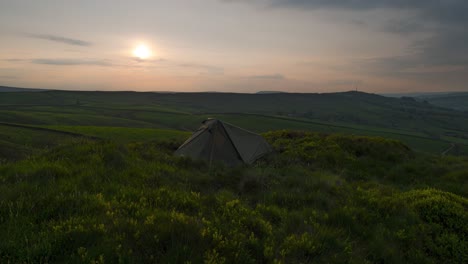 A-phenomenal-timelapse-clip-of-a-sunset-over-a-tent,-that-is-equipped-on-puffy-vivid-green-grass