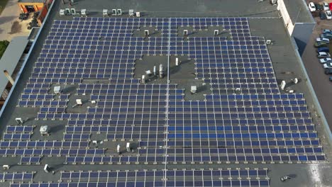 Aerial-shot-of-the-solar-panels-on-a-production-building-roof-on-a-sunny-day,-zooming-in