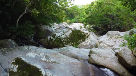 Flight-over-forest-waterfall,-water-flowing-downstream-on-stones,-aerial