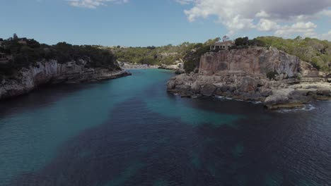 Turquoise-blue-lagoon-Cala-Llombards-in-Mallorca,-aerial-with-sail-boat