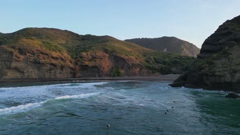 Surfers-waiting-to-catch-waves-while-the-sunset-takes-place-over-Piha-Beach