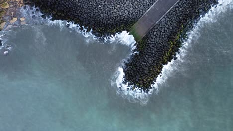 Rising-drone-shot-of-concrete-slipway-surrounded-by-rocky-sea-defences