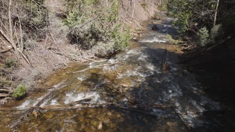 Flowing-creek-in-Owen-Sound-surrounded-by-lush-trees-and-rocky-terrain,-aerial-view