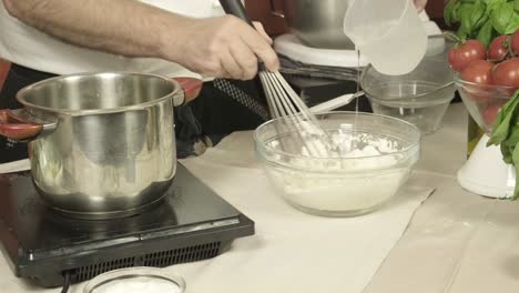 Closeup-hands-of-chef-add-water-to-flour-mixture-Italian-kitchen,-tomatoes-basil