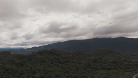 Aerial-drones-fly-over-forests-and-green-hills,-dramatic-clouds