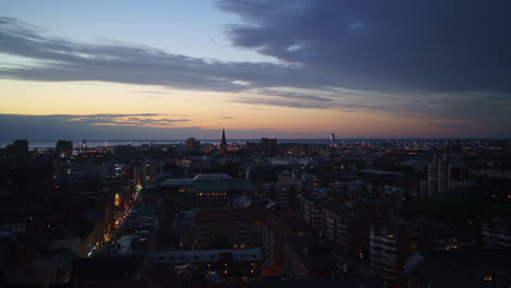 Eine-Wunderschöne-Aufnahme-Der-Skyline-Von-Malmö-In-Diesem-Zeitraffer-Des-Sonnenuntergangs,-Die-Den-Übergang-Der-Stadt-Vom-Tag-Zur-Nacht-Mit-Dem-Öresund-Im-Hintergrund-Festhält