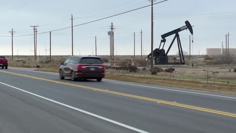 Oil-well-pumping-along-busy-highway,-rising-aerial-shot